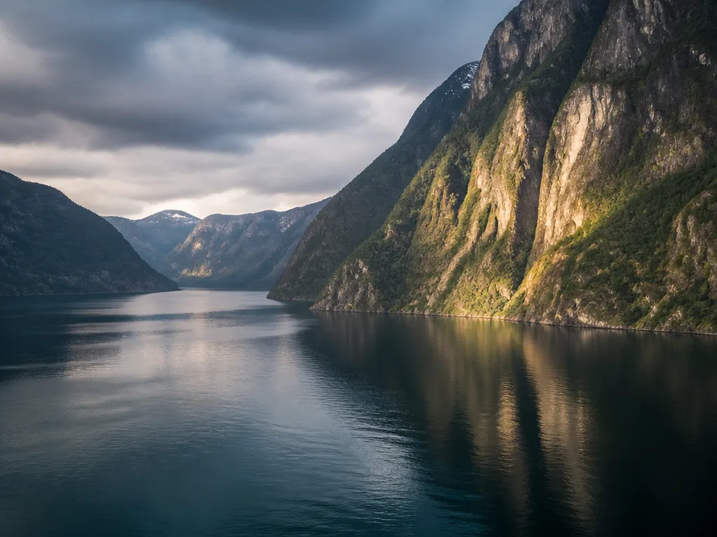 Norsk fjordlandskap med dramatiska bergklippor som speglar sig i stilla mörkblått vatten under ett molnigt himmel